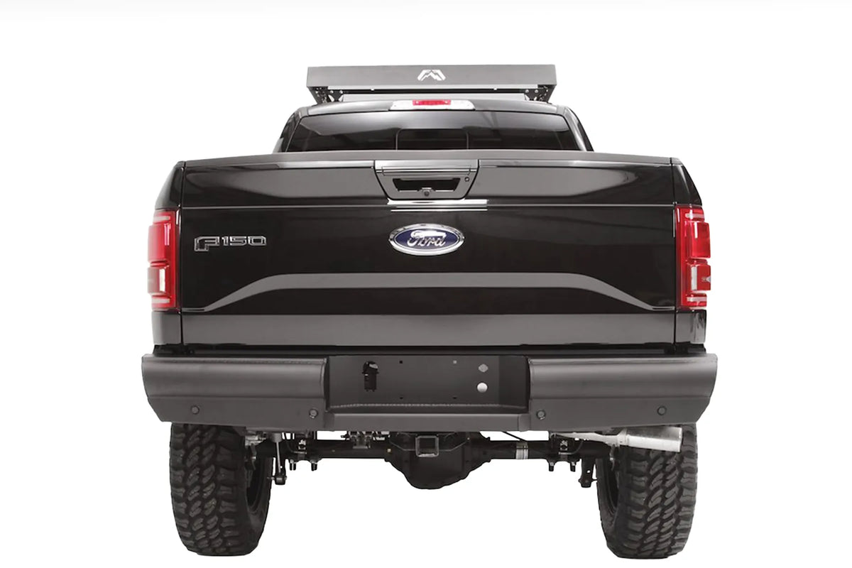 Fab Fours Black Steel Elite rear bumper on a black Ford F-150, straight-on rear view, showing the smooth full-width bumper, license plate recess and receiver hitch