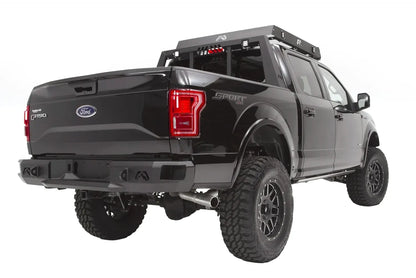 Fab Fours Premium rear bumper on a black Ford F-150, rear passenger-side three-quarter view, showing the logo cutouts, wrapped end cap and roof rack