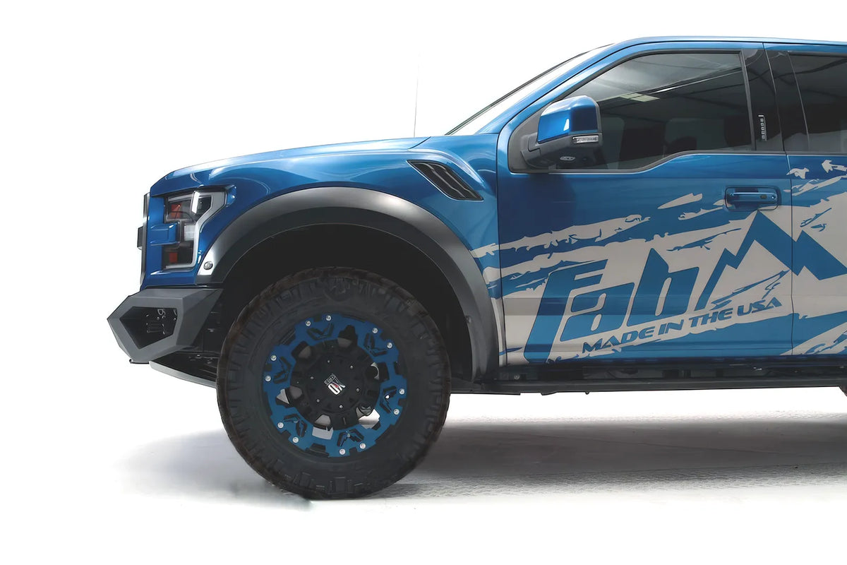 Fab Fours Vengeance front bumper on a blue and gray wrapped Ford Raptor, driver-side profile view, showing the low-profile bumper end and wheel clearance