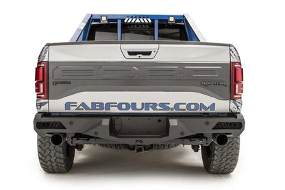 Fab Fours Vengeance rear bumper on a silver and navy wrapped Ford Raptor, straight-on rear view, showing the center plate recess, exhaust cutouts and side light openings
