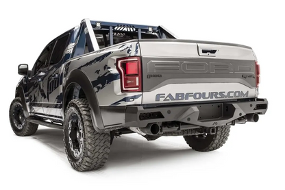 Fab Fours Vengeance rear bumper on a silver and navy wrapped Ford Raptor, rear driver-side three-quarter view, showing the bumper end, exhaust cutouts and light openings