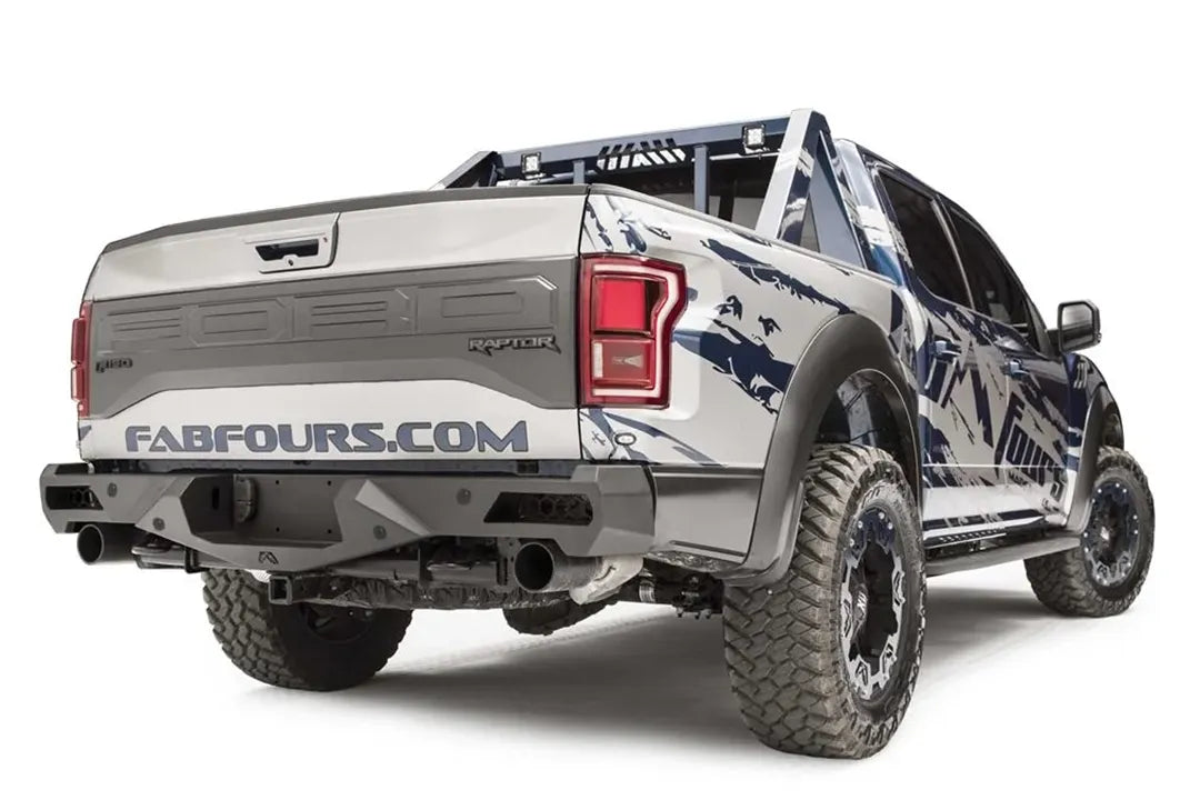 Fab Fours Vengeance rear bumper on a silver and navy wrapped Ford Raptor, rear passenger-side three-quarter view, showing the bumper end, exhaust cutouts and chase rack