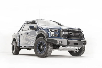 Fab Fours Premium Winch front bumper on a blue and gray wrapped Ford Raptor, front passenger-side three-quarter view, showing the winch recess, round fog lights and bumper ends