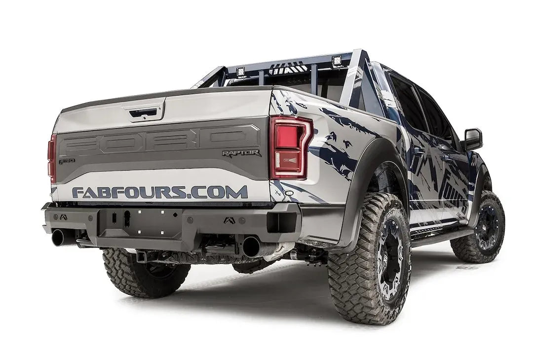 Fab Fours Premium rear bumper on a silver and navy wrapped Ford Raptor, rear passenger-side three-quarter view, showing the logo cutouts, bumper end and chase rack