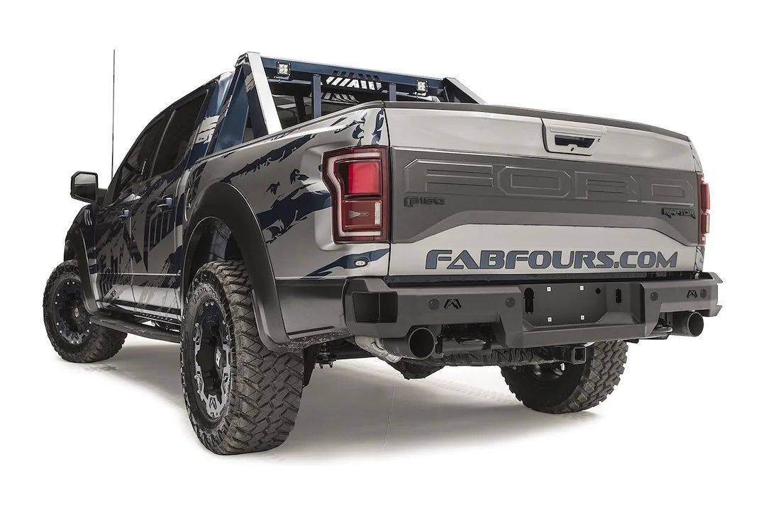 Fab Fours Premium rear bumper on a silver and navy wrapped Ford Raptor, rear driver-side three-quarter view, showing the logo cutouts, sensor-ready face and bumper end