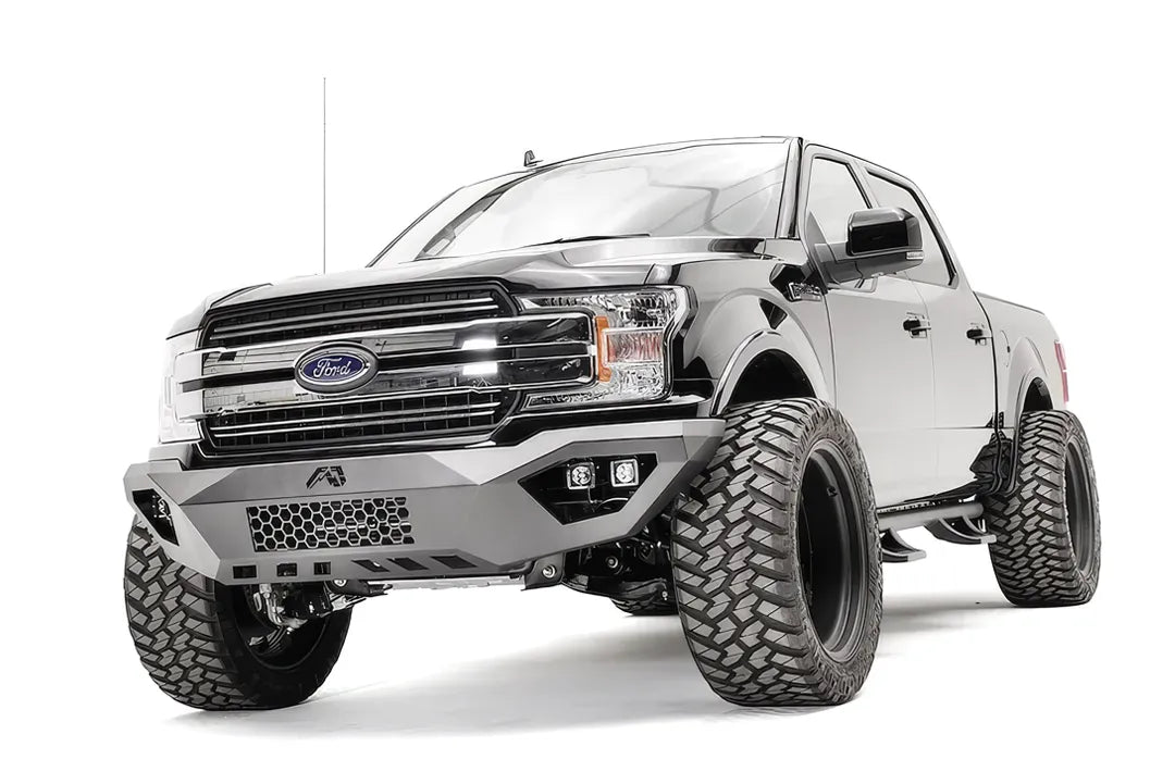 Fab Fours Vengeance front bumper on a black Ford F-150, front driver-side three-quarter view, showing the mesh center panel, cube light pods and skid plate
