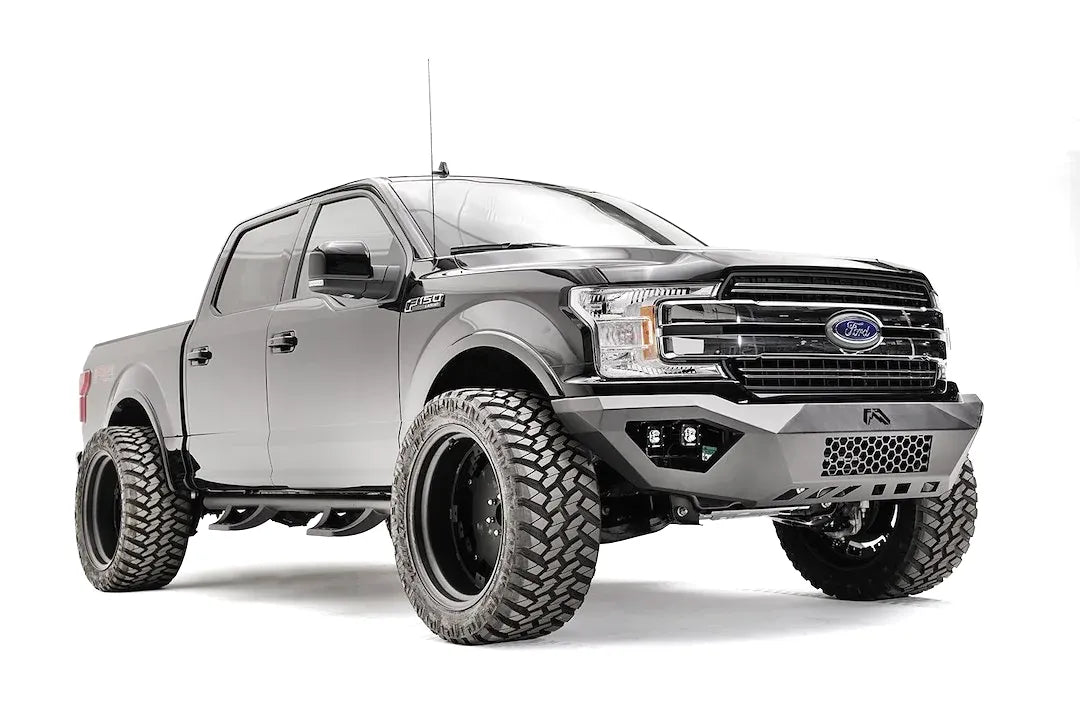 Fab Fours Vengeance front bumper on a black Ford F-150, front passenger-side three-quarter view, showing the mesh center panel, cube light pods and angled end caps