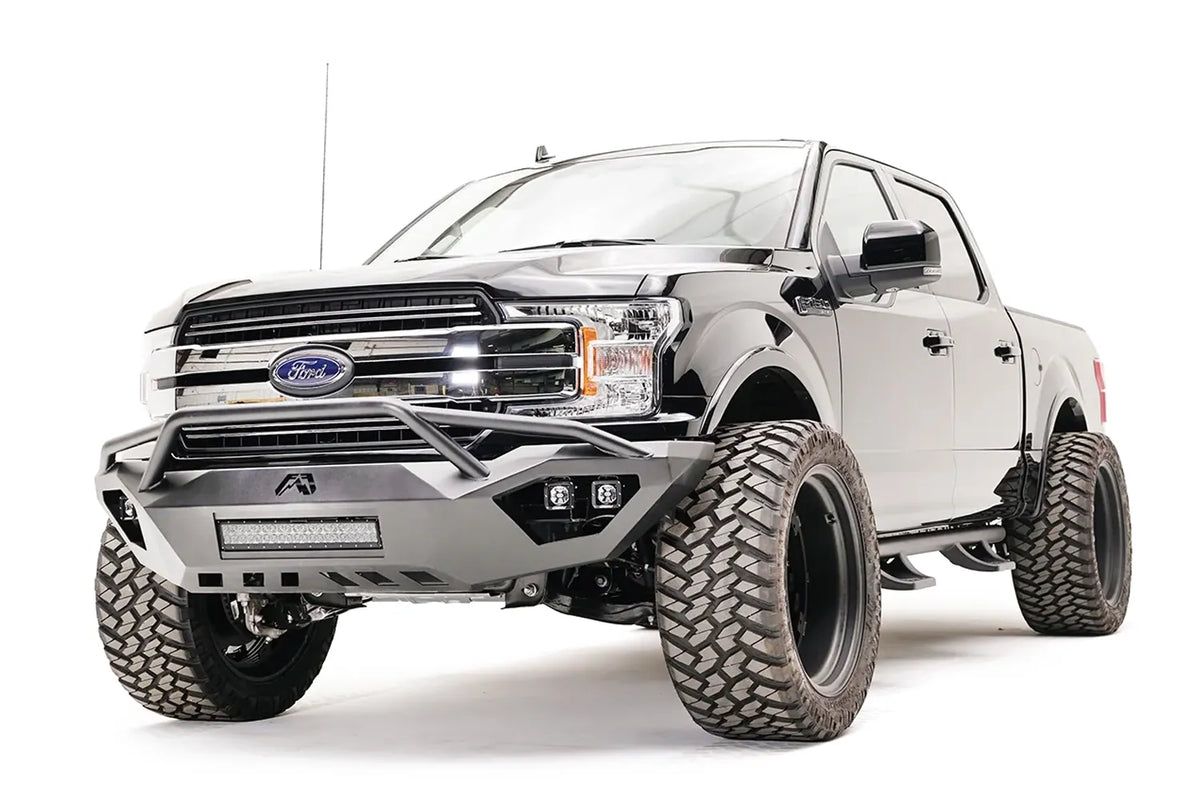 Fab Fours Vengeance front bumper with pre-runner guard on a black Ford F-150, front driver-side three-quarter view, showing the pre-runner hoop, light bar and cube light pods