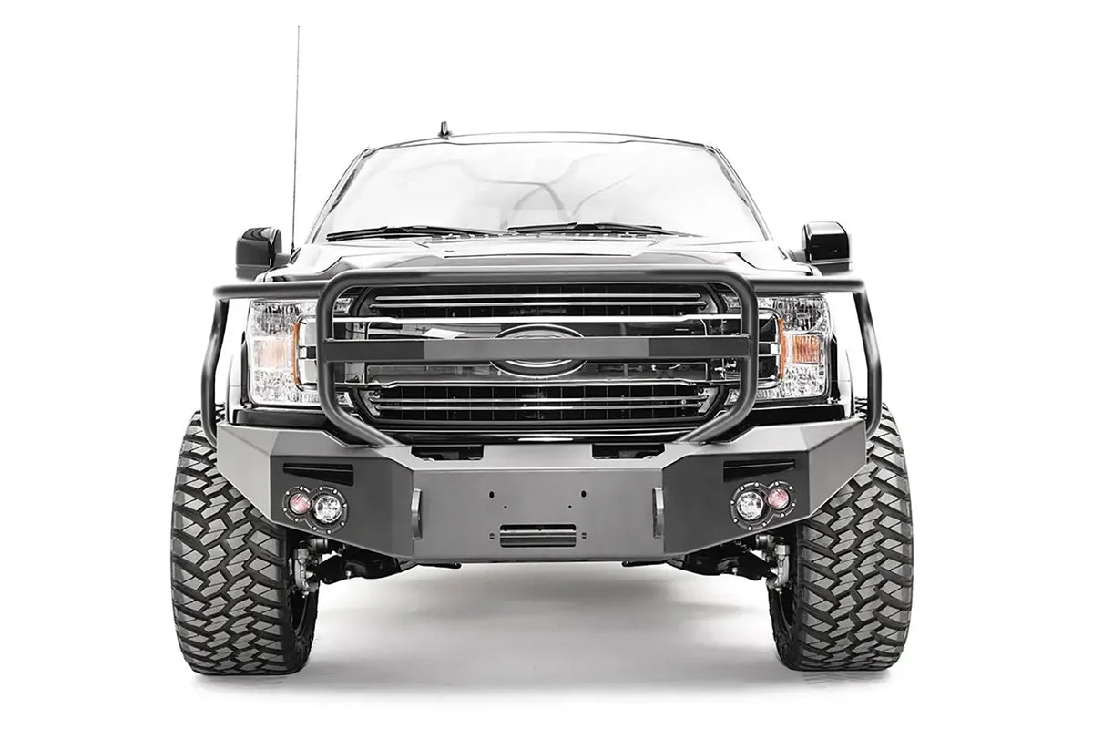 Fab Fours Premium Winch front bumper with full guard on a black Ford F-150, straight-on front view, showing the full grille guard, winch recess and round fog lights