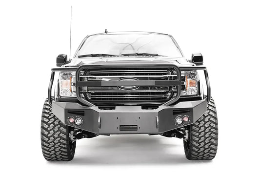 Fab Fours Premium Winch front bumper with full guard on a black Ford F-150, straight-on front view, showing the full grille guard, winch recess and round fog lights