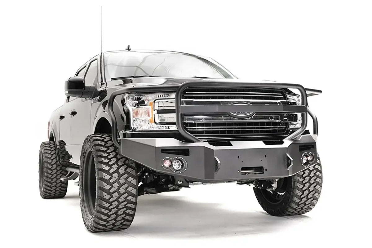 Fab Fours Premium Winch front bumper with full guard on a black Ford F-150, front passenger-side three-quarter view, showing the full grille guard, winch recess and round fog lights