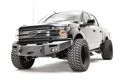 Fab Fours Premium Winch front bumper on a black Ford F-150, front driver-side three-quarter view, showing the winch recess, round fog lights and bumper ends