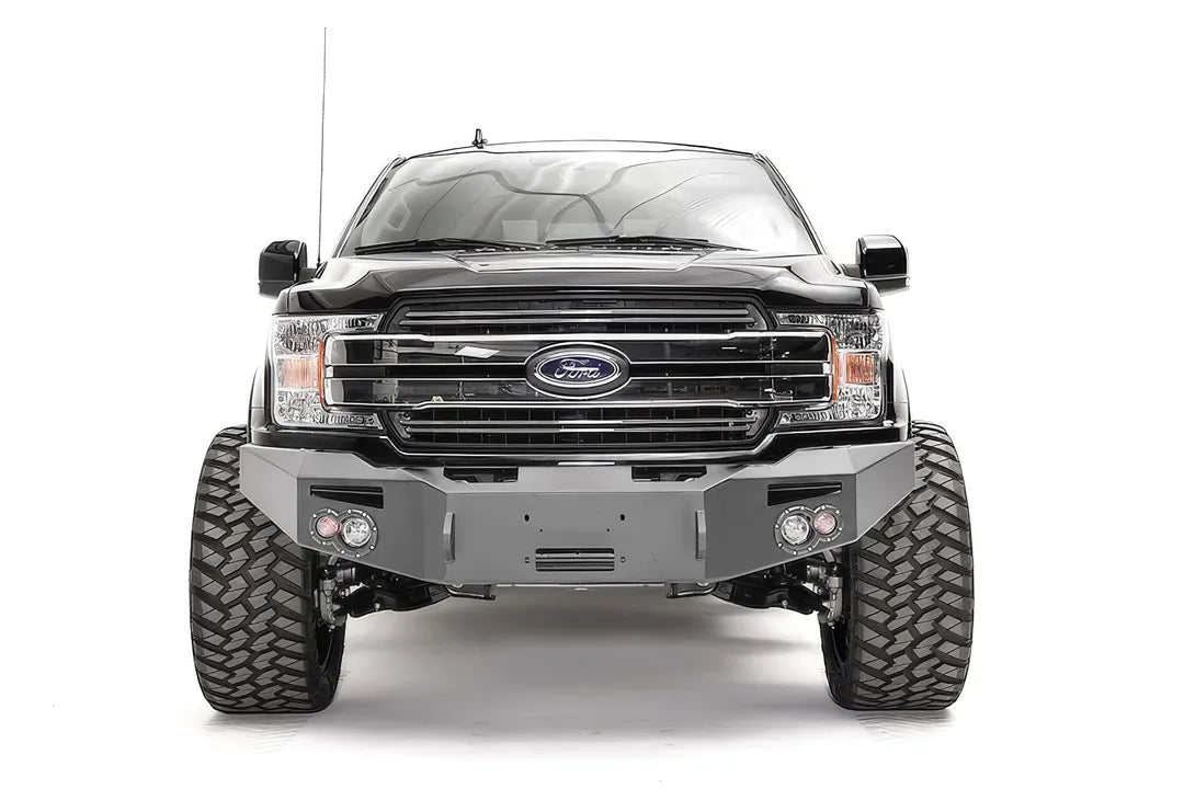 Fab Fours Premium Winch front bumper on a black Ford F-150, straight-on front view, showing the center winch recess, round fog lights and shackle mounts