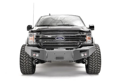 Fab Fours Premium Winch front bumper on a black Ford F-150, straight-on front view, showing the center winch recess, round fog lights and shackle mounts