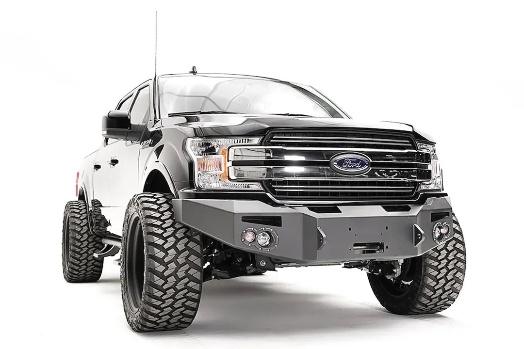 Fab Fours Premium Winch front bumper on a black Ford F-150, front passenger-side three-quarter view, showing the winch recess, round fog lights and bumper ends