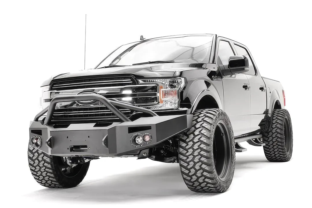 Fab Fours Premium Winch front bumper with pre-runner guard on a black Ford F-150, front driver-side three-quarter view, showing the pre-runner hoop, winch recess and round fog lights