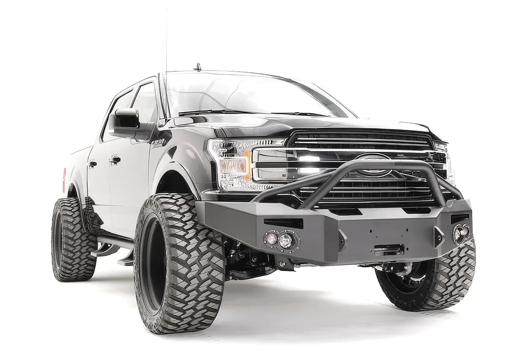 Fab Fours Premium Winch front bumper with pre-runner guard on a black Ford F-150, front passenger-side three-quarter view, showing the pre-runner hoop, winch recess and round fog lights