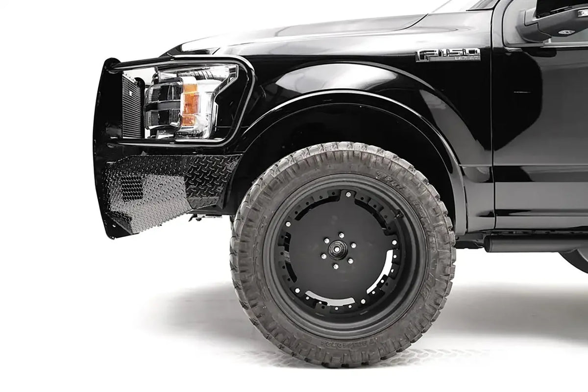 Fab Fours Black Steel front bumper with full guard on a black Ford F-150, close-up of the front corner, showing the guard upright, diamond-plate bumper end and wheel clearance