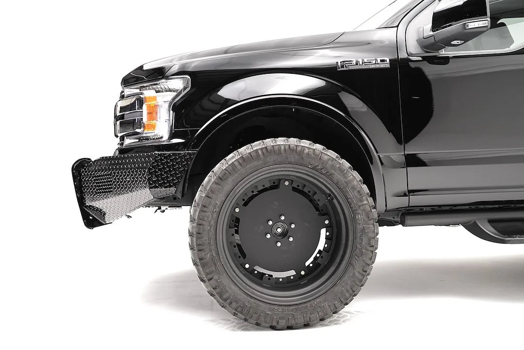 Fab Fours Black Steel front bumper on a black Ford F-150, close-up of the front corner, showing the diamond-plate bumper end and wheel clearance