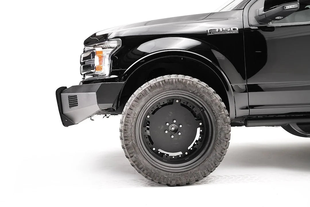 Fab Fours Black Steel Elite front bumper on a black Ford F-150, close-up of the front corner, showing the bumper end, mesh vent and wheel clearance