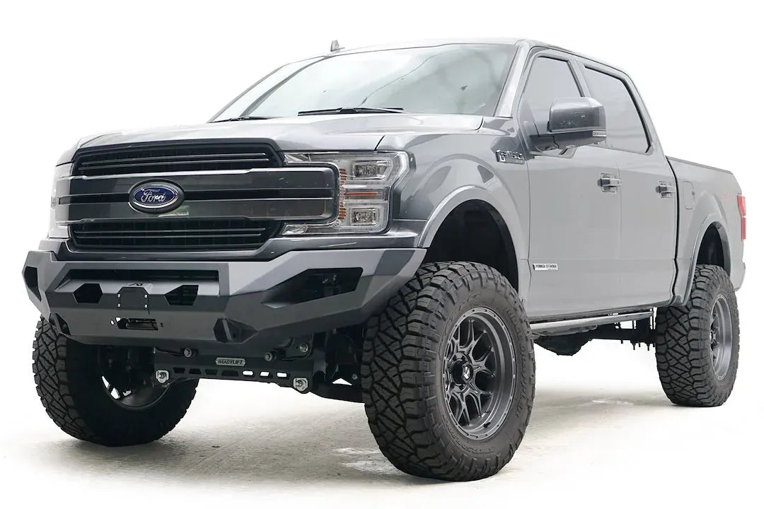 Fab Fours Matrix front bumper on a gray Ford F-150, front driver-side three-quarter view, showing the winch, cube light openings and angled end caps