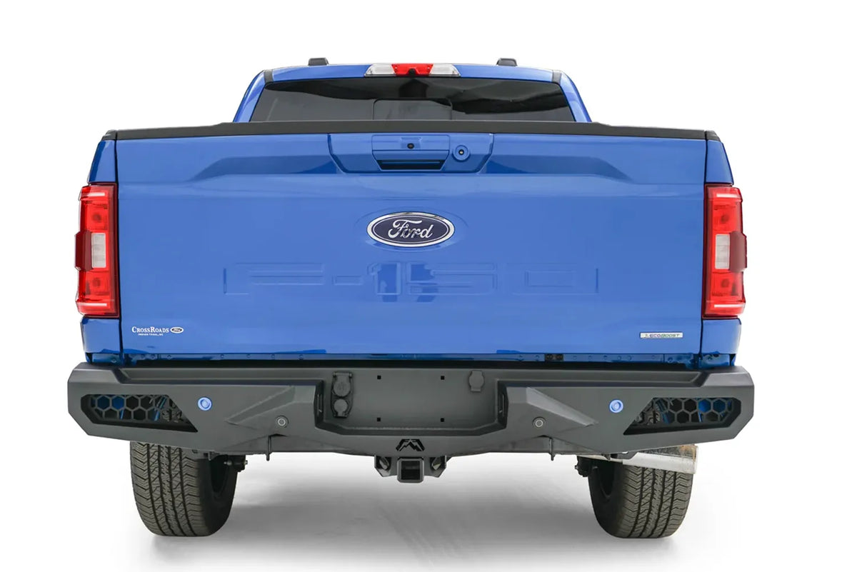Fab Fours Vengeance rear bumper on a blue Ford F-150, straight-on rear view, showing the honeycomb light cutouts, sensor holes and center hitch recess