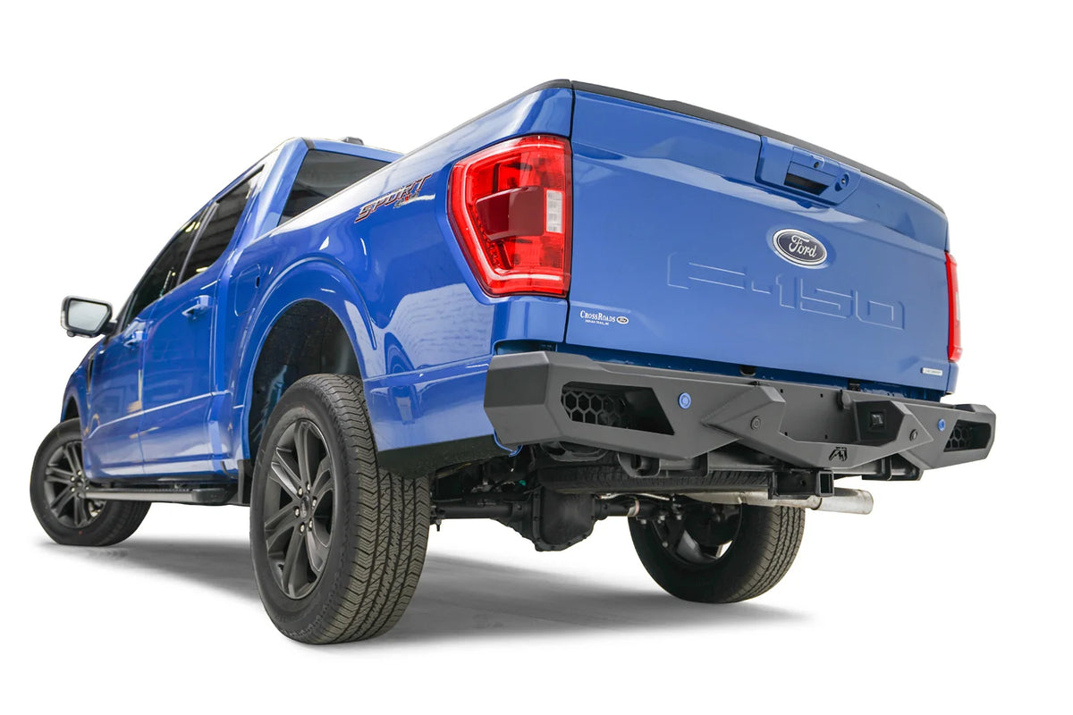 Fab Fours Vengeance rear bumper on a blue Ford F-150, rear driver-side three-quarter view, showing the honeycomb cutouts, sensor holes and angled end cap