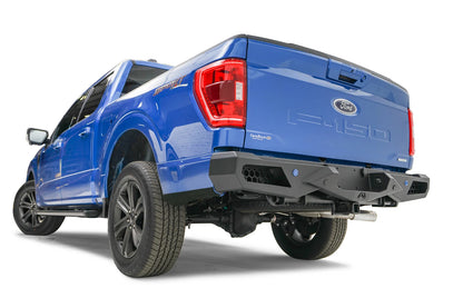 Fab Fours Vengeance rear bumper on a blue Ford F-150, rear driver-side three-quarter view, showing the honeycomb cutouts, sensor holes and angled end cap