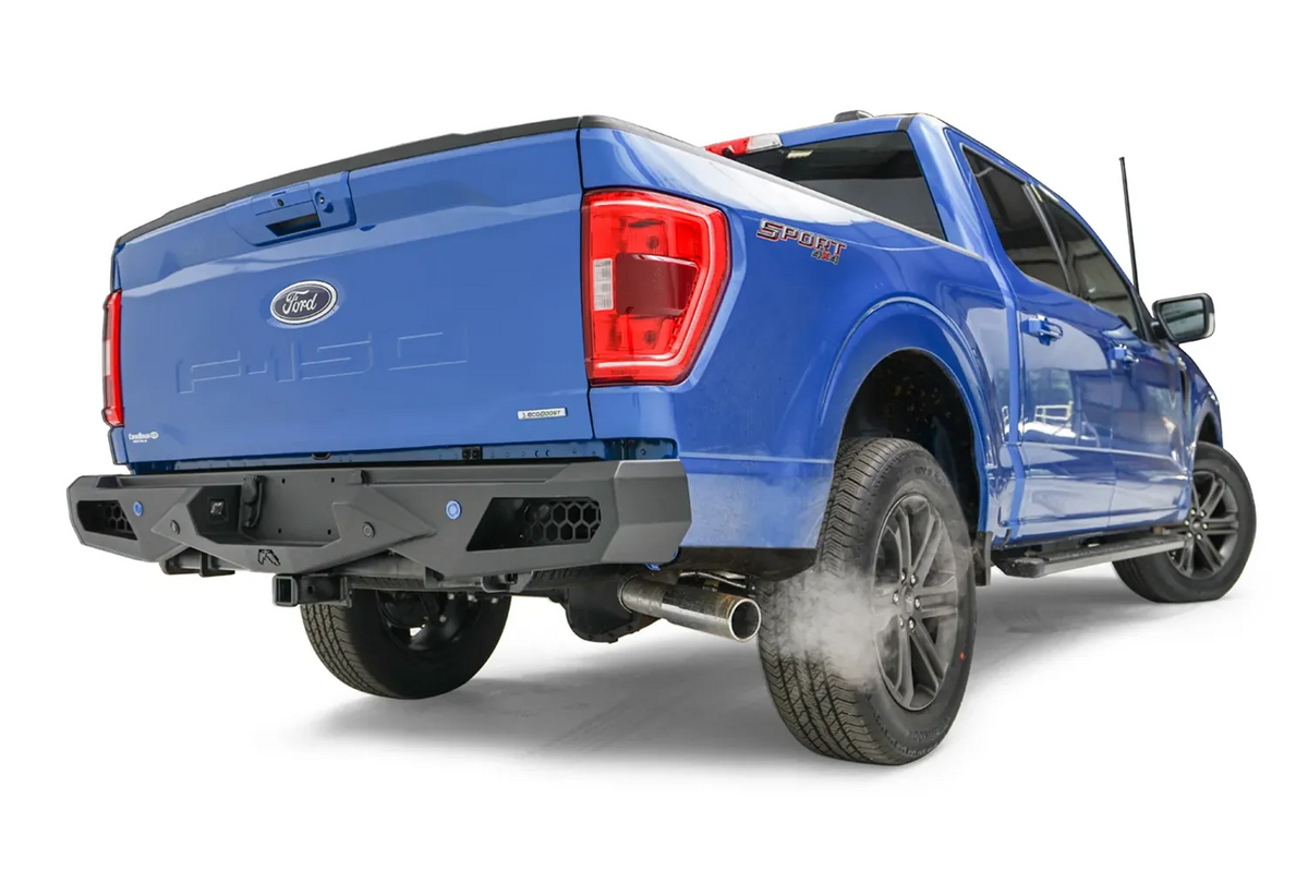 Fab Fours Vengeance rear bumper on a blue Ford F-150, rear passenger-side three-quarter view, showing the honeycomb cutouts, sensor holes and angled end cap