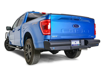 Fab Fours Black Steel Elite rear bumper on a blue Ford F-150, rear driver-side three-quarter view, showing the wrapped bumper end, sensor holes and plate recess