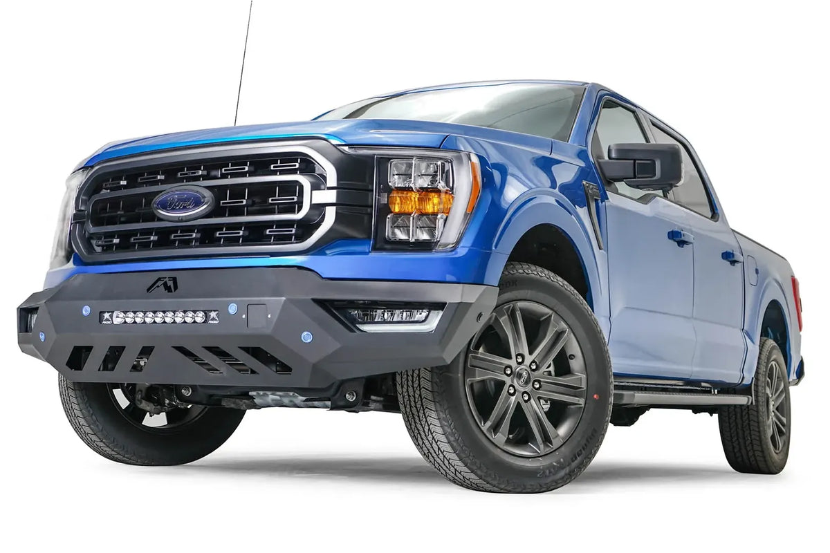 Fab Fours Vengeance front bumper on a blue Ford F-150, front driver-side three-quarter view, showing the light bar, angled end cap and skid plate cutouts