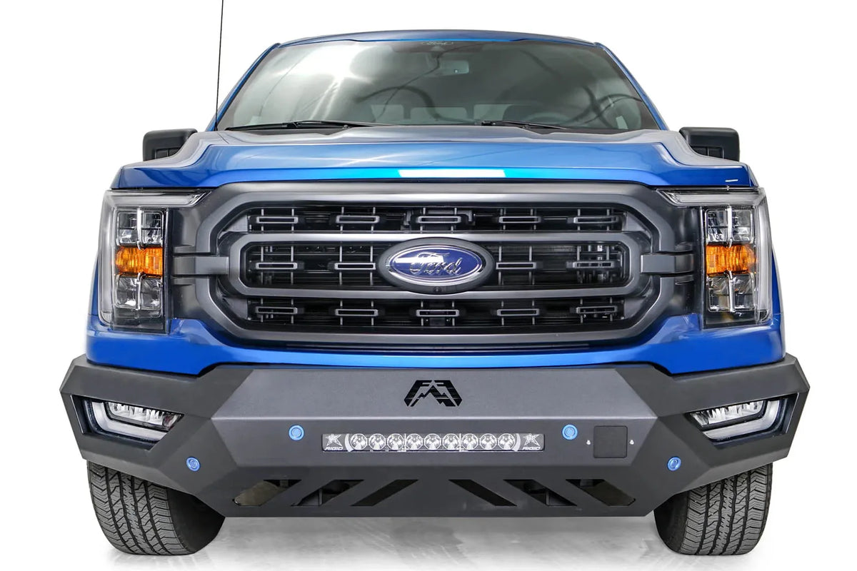 Fab Fours Vengeance front bumper on a blue Ford F-150, straight-on front view, showing the center light bar, sensor holes and angled skid plate