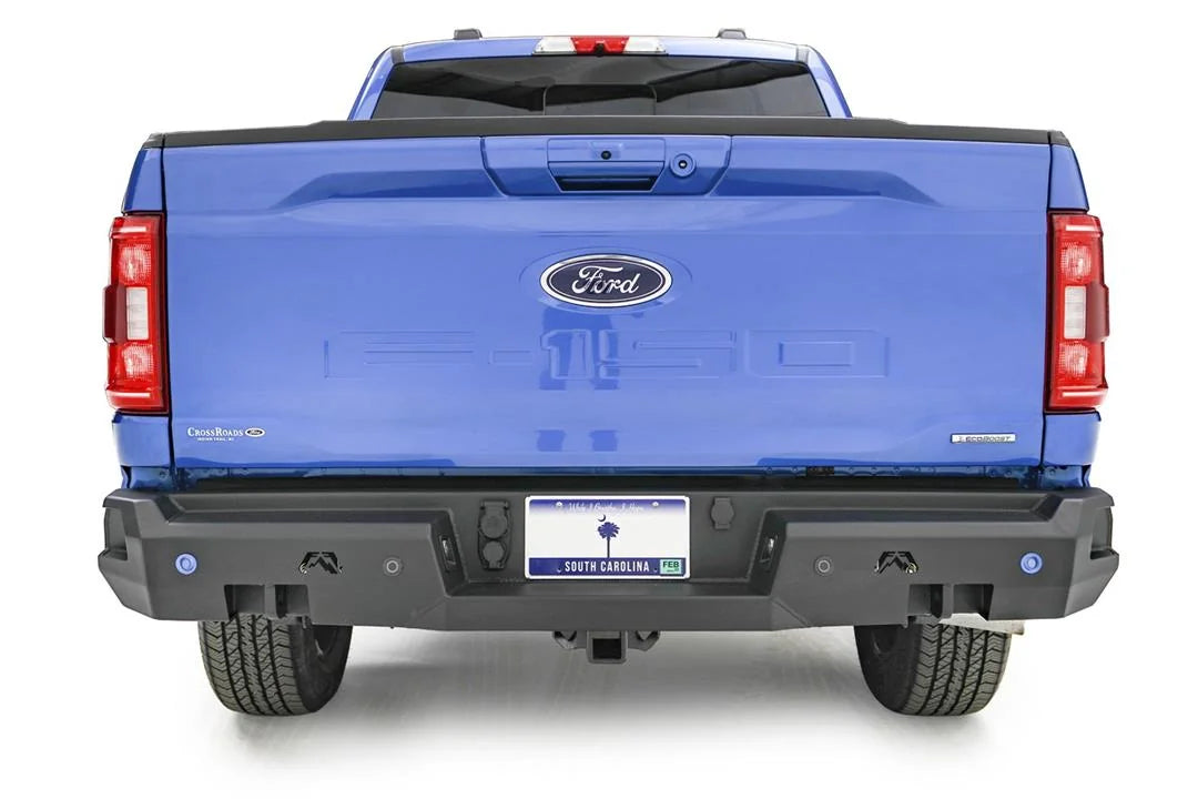 Fab Fours Premium rear bumper on a blue Ford F-150, straight-on rear view, showing the logo cutouts, sensor holes and center plate recess