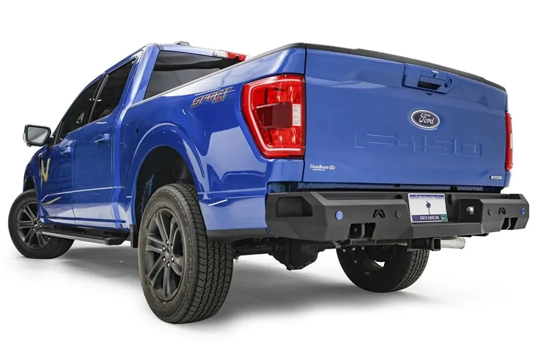 Fab Fours Premium rear bumper on a blue Ford F-150, rear driver-side three-quarter view, showing the logo cutouts, sensor holes and bumper end