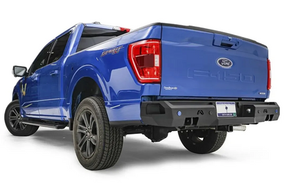 Fab Fours Premium rear bumper on a blue Ford F-150, rear driver-side three-quarter view, showing the logo cutouts, sensor holes and bumper end