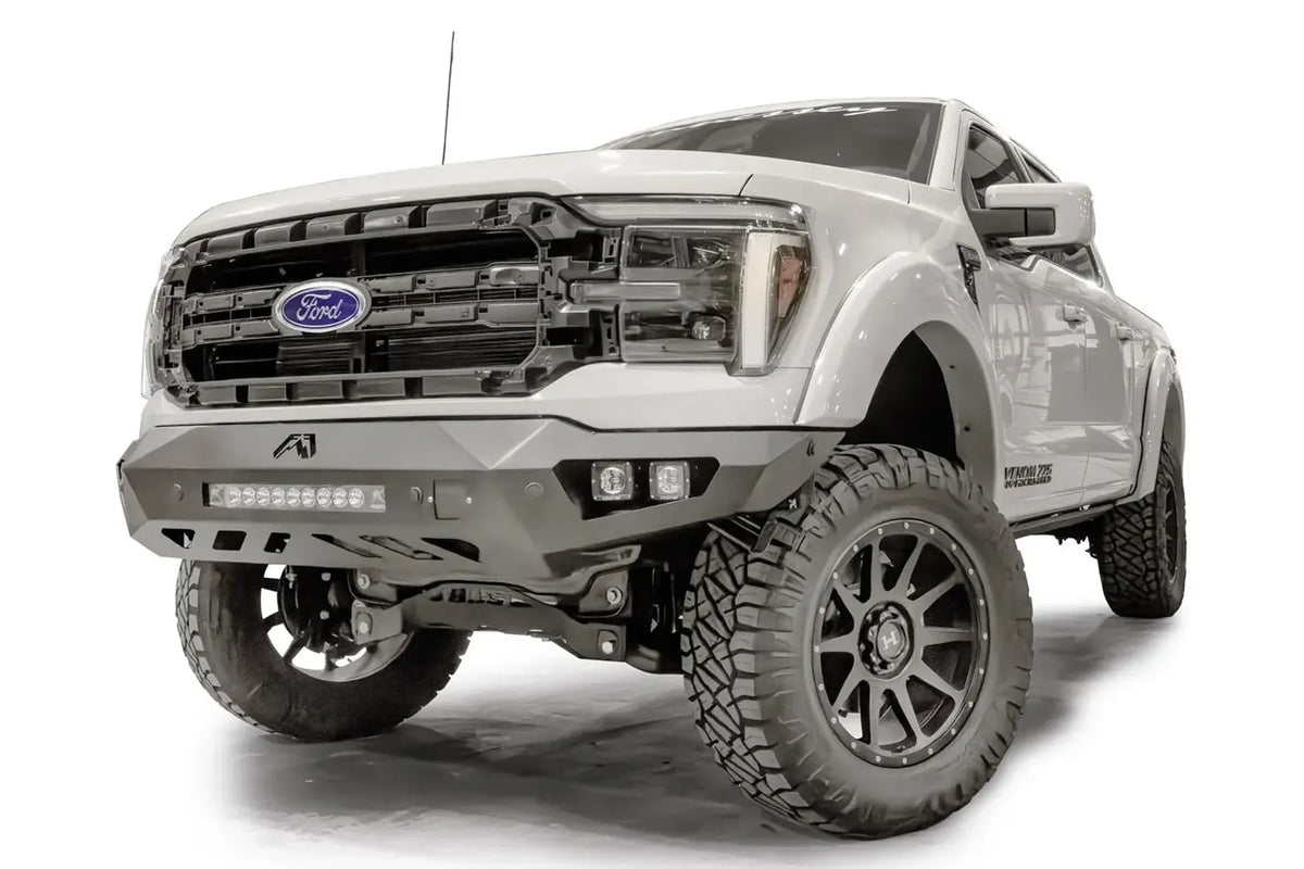 Fab Fours Vengeance front bumper on a white Ford F-150, front driver-side three-quarter view, showing the light bar, cube light pods and angled end cap