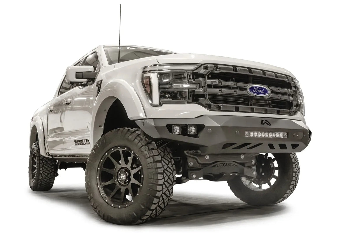 Fab Fours Vengeance front bumper on a white Ford F-150, front passenger-side three-quarter view, showing the light bar, cube light pods and skid plate