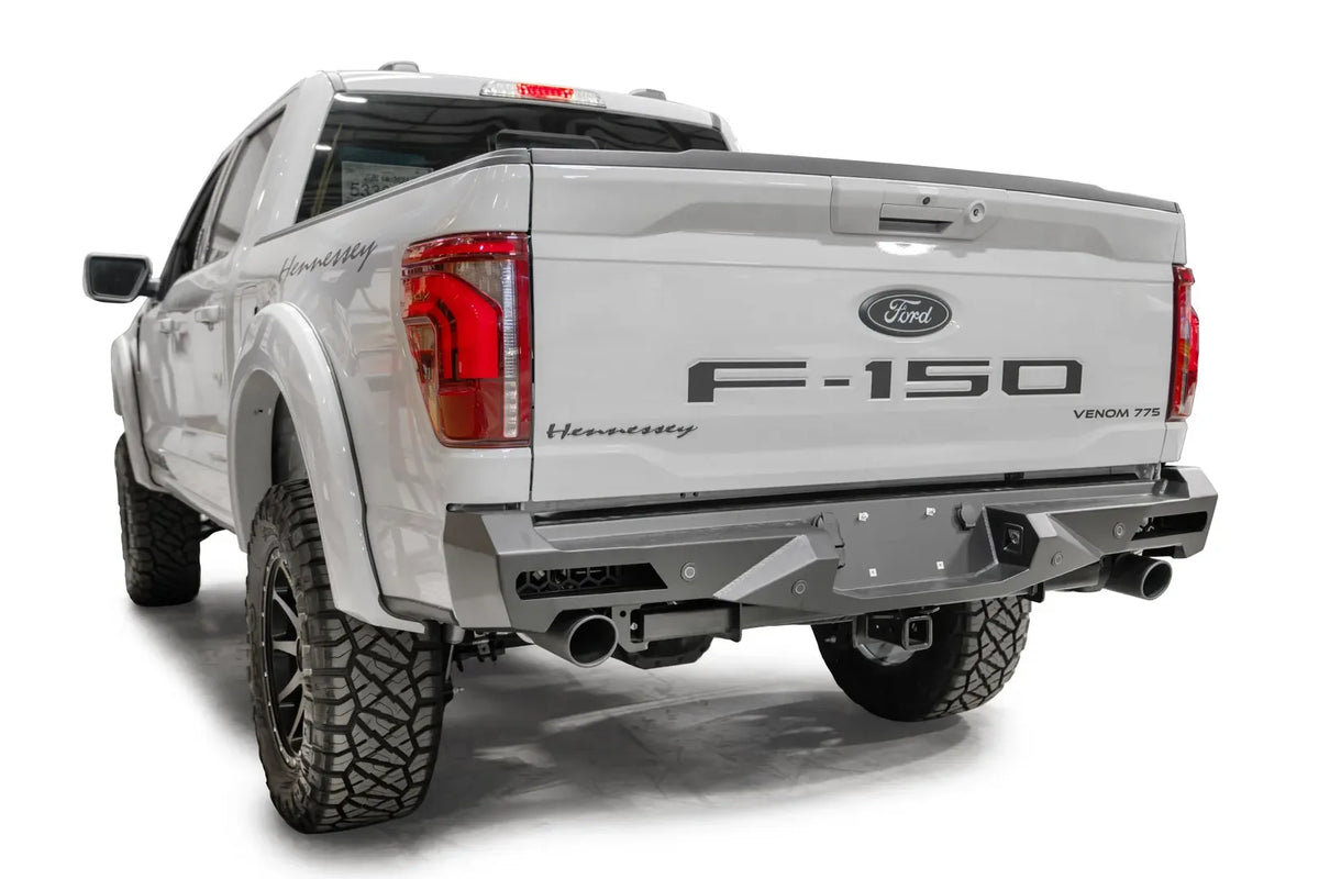 Fab Fours Vengeance rear bumper on a white Ford F-150, rear driver-side three-quarter view, showing the angled end cap, light cutouts and exhaust openings