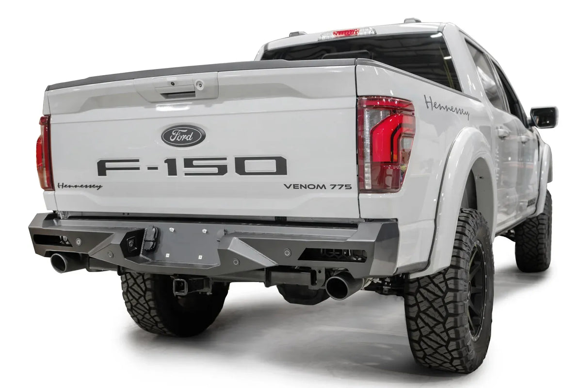 Fab Fours Vengeance rear bumper on a white Ford F-150, rear passenger-side three-quarter view, showing the angled end cap, light cutouts and exhaust openings