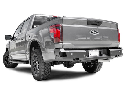 Fab Fours Premium rear bumper on a gray Ford F-150, rear driver side view, showing the sensor cutouts, the corner step pads and the integrated hitch receiver opening