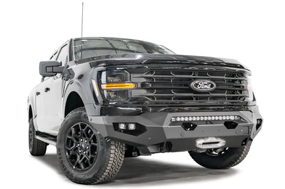 Fab Fours Matrix front bumper on a black Ford F-150, front driver-side three-quarter view, showing the light bar, winch fairlead and cube light pods