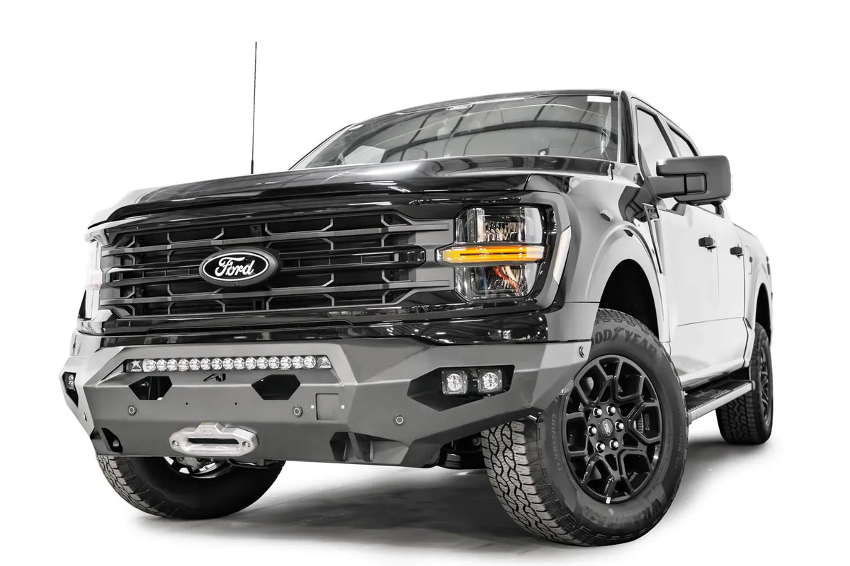 Fab Fours Matrix front bumper on a black Ford F-150, front passenger-side three-quarter view, showing the light bar, winch fairlead and angled end cap