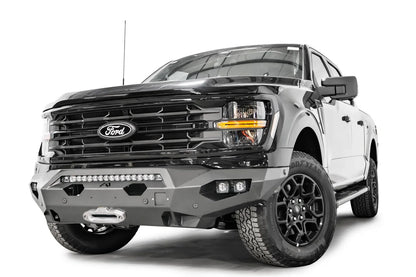 Fab Fours Matrix front bumper on a black Ford F-150, front passenger-side three-quarter view, showing the light bar, winch fairlead and angled end cap