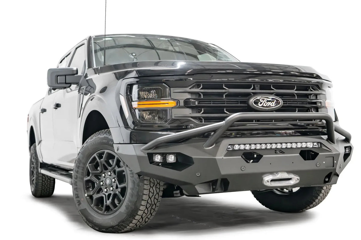 Fab Fours Matrix front bumper with pre-runner guard on a black Ford F-150, front driver-side three-quarter view, showing the pre-runner hoop, light bar and winch fairlead