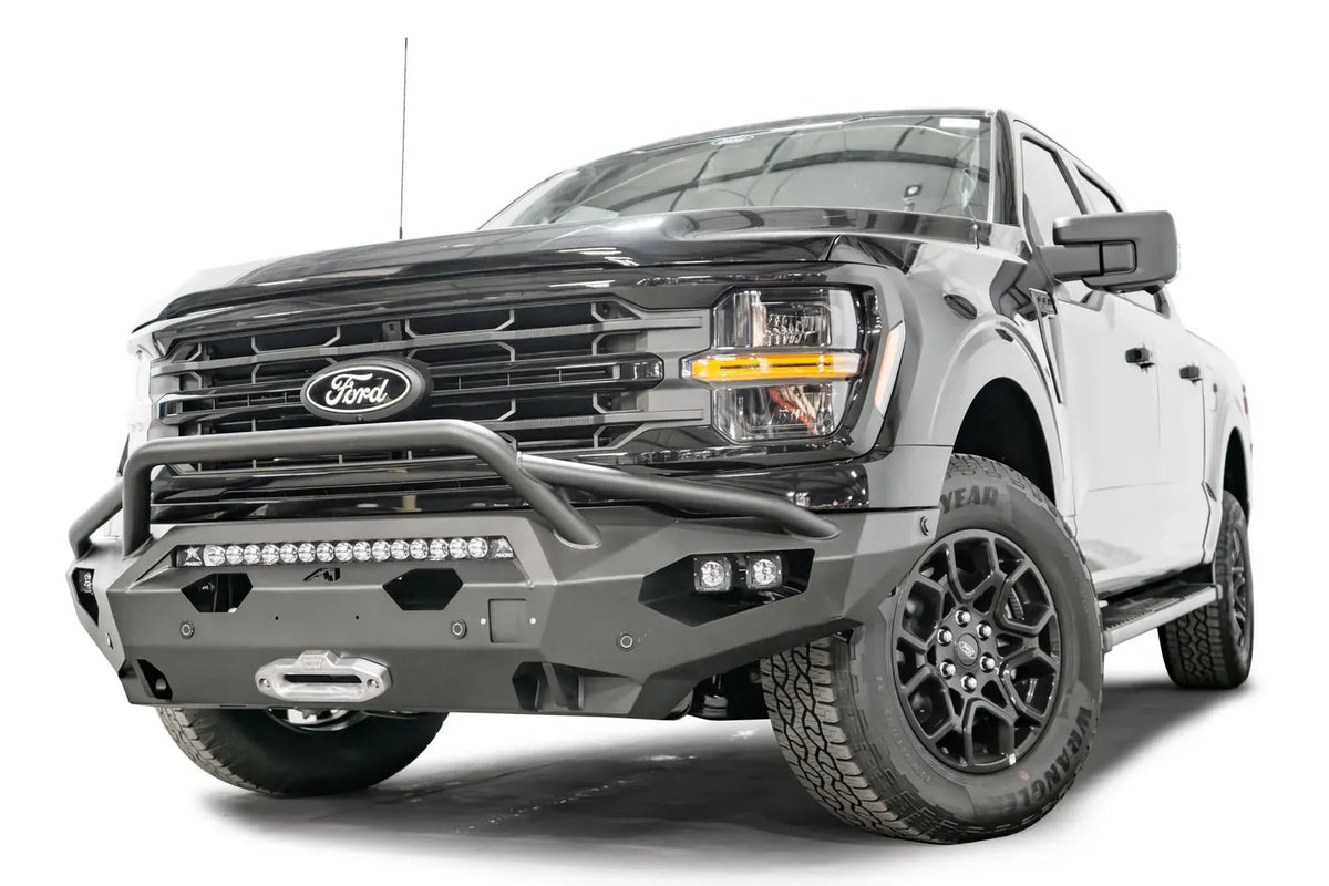 Fab Fours Matrix front bumper with pre-runner guard on a black Ford F-150, front driver-side three-quarter view, showing the pre-runner hoop, light bar and winch fairlead