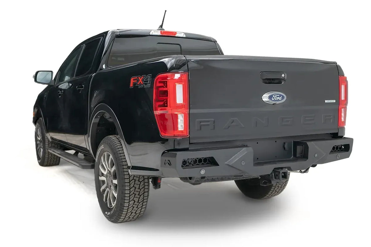 Fab Fours Vengeance rear bumper with honeycomb mesh corner openings on a black Ford Ranger, driver-side rear three-quarter view, with parking sensors and hitch receiver