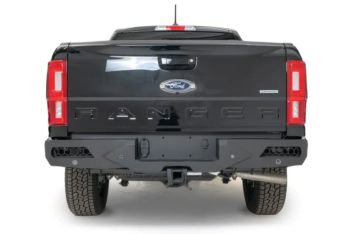 Fab Fours Vengeance rear bumper on a black Ford Ranger, straight rear view, with honeycomb mesh corner openings, parking sensors, center license plate mount, and hitch receiver
