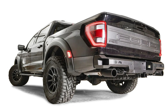 Fab Fours Premium rear bumper on a dark gray Ford F-150 Raptor, rear driver-side three-quarter view, showing the bumper end cap, Fab Fours logo plate and exhaust cutout
