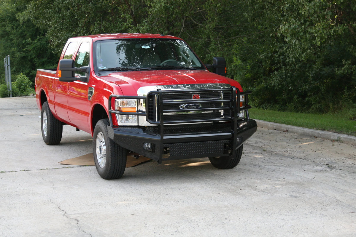 Fab Fours Black Steel front ranch bumper with full guard on a red Ford Super Duty outdoors, front passenger-side three-quarter view, showing the full tubular grille guard, diamond-plate face and bumper wing