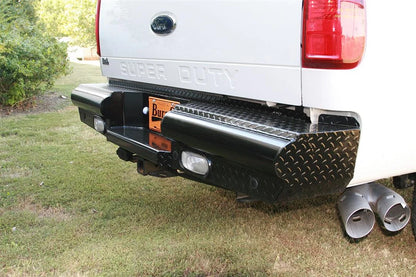 Fab Fours Black Steel ranch rear bumper on a white Ford Super Duty outdoors, close-up of the rear corner, showing the diamond-plate top step, end cap and light cutout
